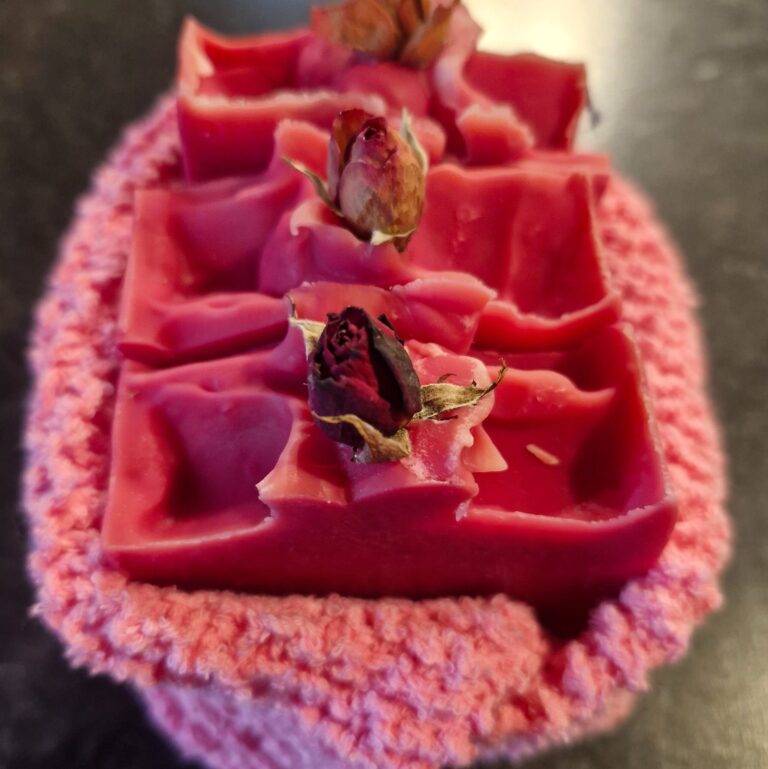 Three FatglowWild Bloom tallow soaps arranged with fresh roses on top, wrapped in soft pink knitted cloth