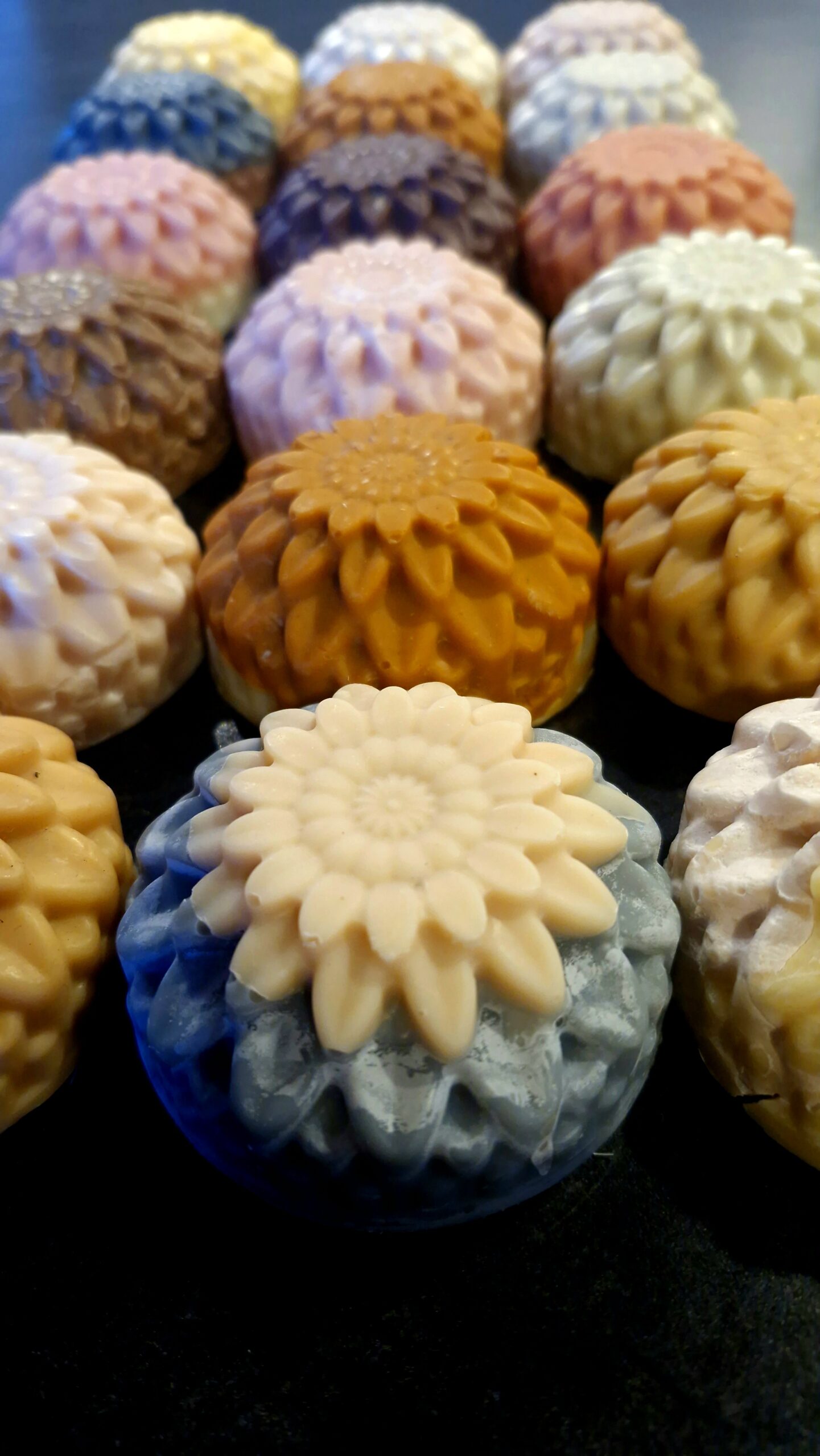 A colourful array of dahlia-embossed round tallow soaps in varied natural hues, handmade by Fatglow